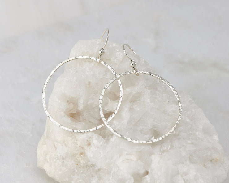 Silver large hammered hoop earrings on white rock