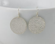 Silver disc earrings hanging from a white cup