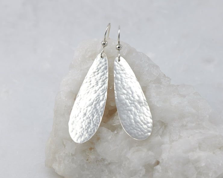 Silver dangle hammered teardrop earrings on white rock