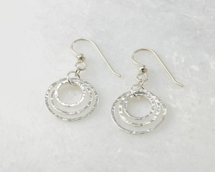 Silver polished hammered hoop earrings on white marble