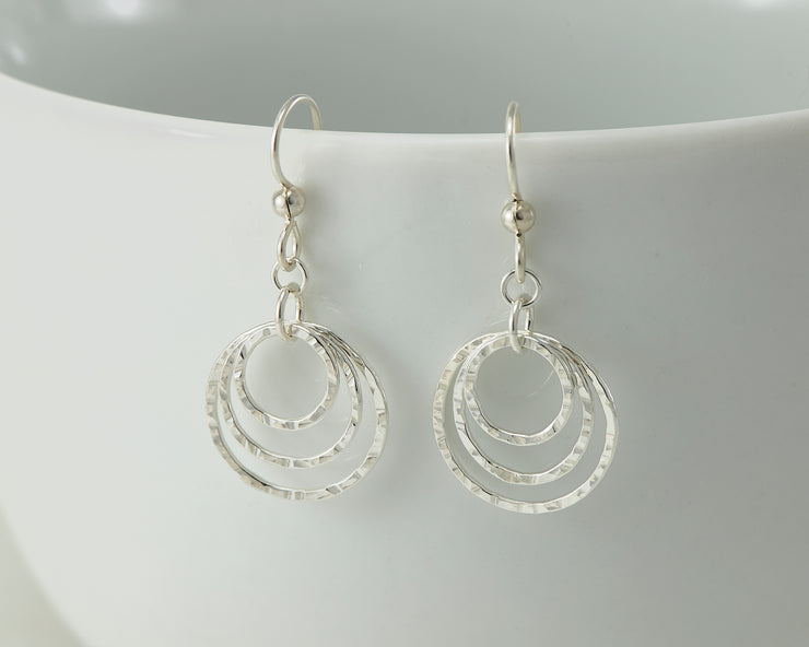 Silver hammered hoop earrings on white cup