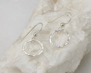 Silver dangle hammered hoop earrings on white rock