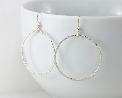 Silver large hammered hoop earrings on white cup