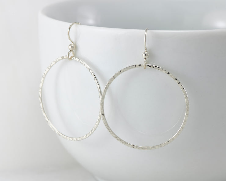 Silver large hammered hoop earrings on white cup