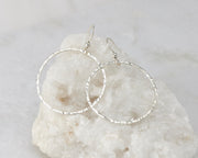 Silver large hammered hoop earrings on white rock