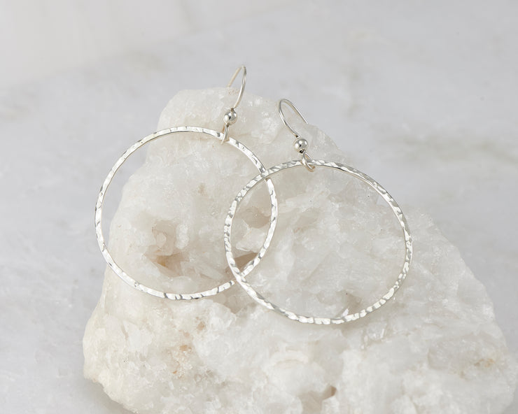 Silver large hammered hoop earrings on white rock