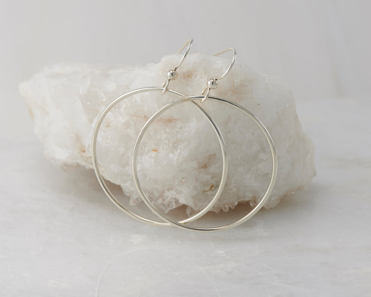 Silver dangle large hoop earrings on white rock