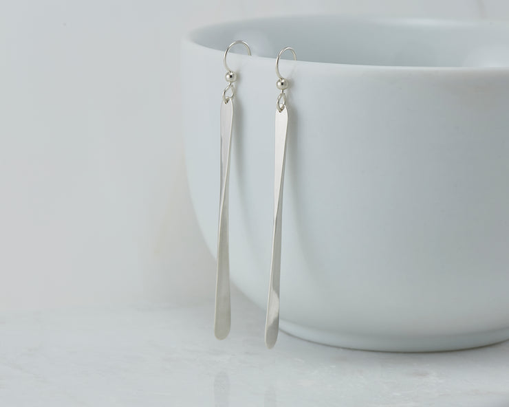 long silver bar earrings on white cup