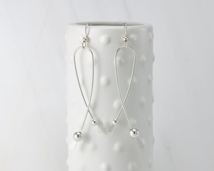 Silver long curved earrings on dotted vase