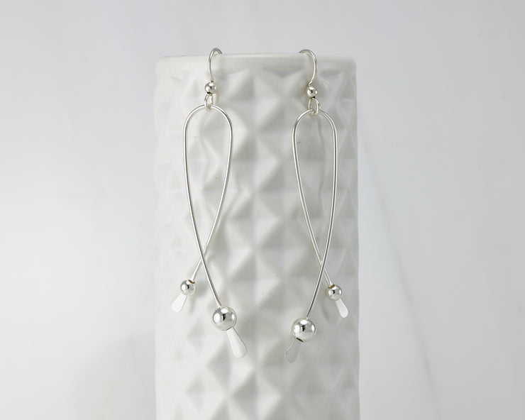 Silver long curved earrings on geometric vase