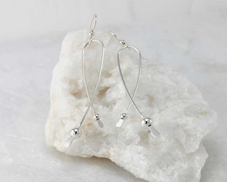 Silver long curved earrings on white rock