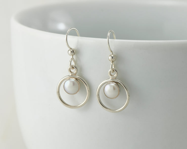 Silver pearl hoop earrings on white cup