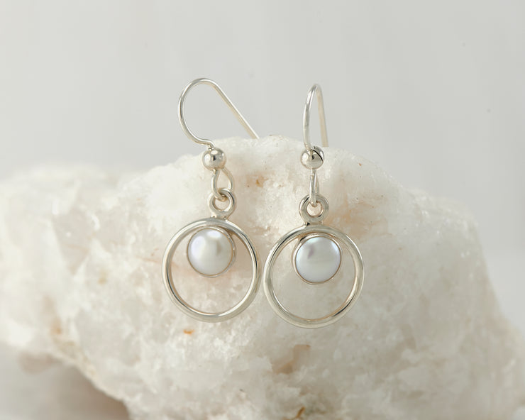 Silver pearl hoop earrings on white rock