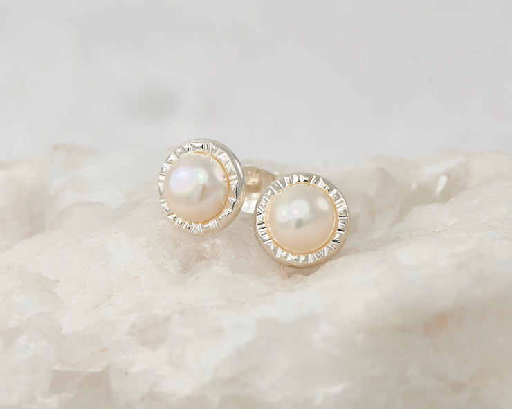 Silver dangle pearl stud earrings on white rock