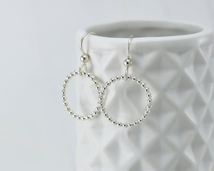 Silver beaded circle hoop earrings on geometric vase
