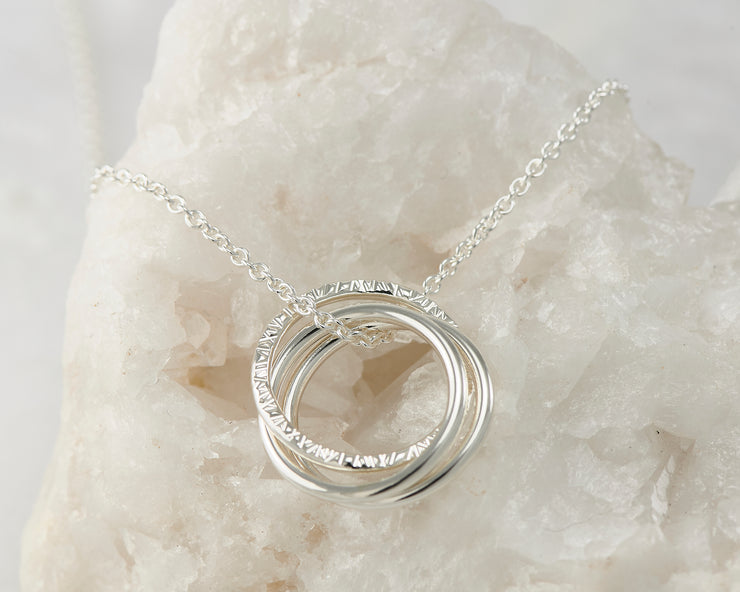 Silver interlocking unity necklace on white rock