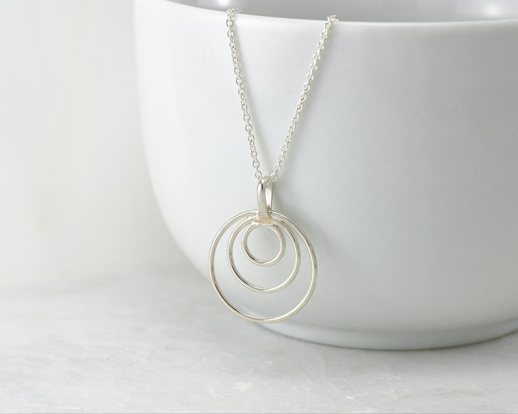 silver circles necklace hanging from white cup