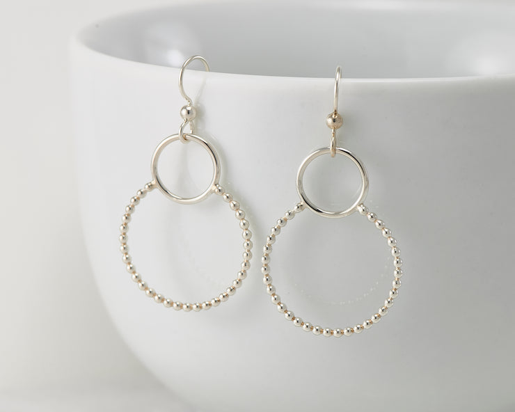 Silver beaded circles hoop earrings on white cup