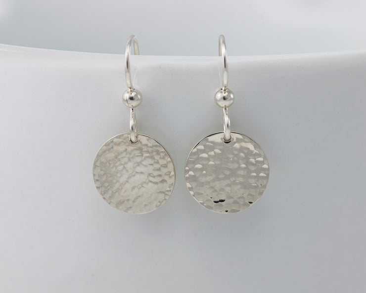 Silver disc earrings hanging from a white cup