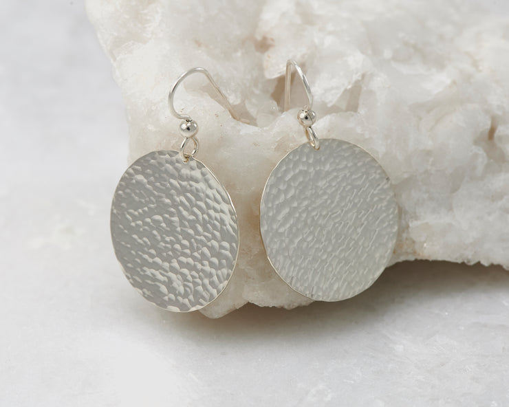 Hammered Dangle Earrings shown on a white rock