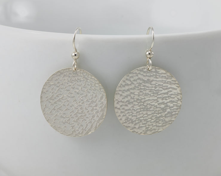 Silver disc earrings hanging from a white cup