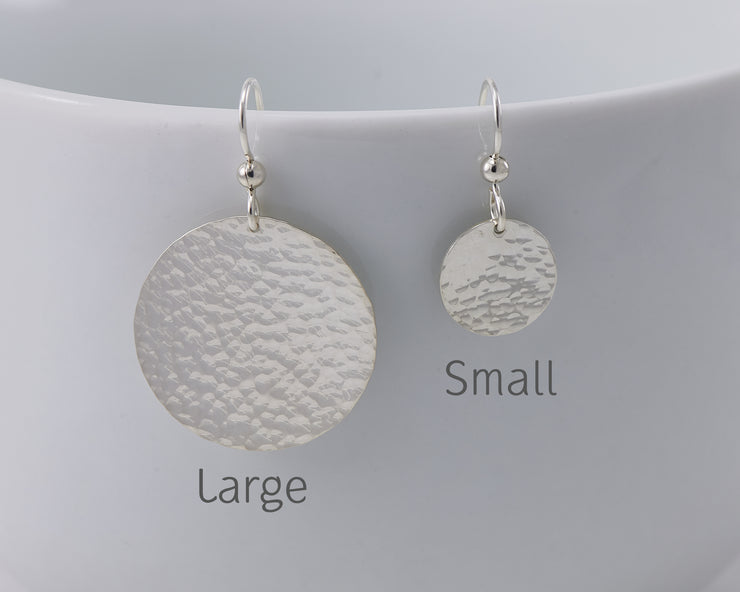 Large and Small hammered silver earrings hanging from a cup