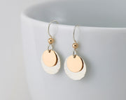 silver and gold disc earrings on white cup
