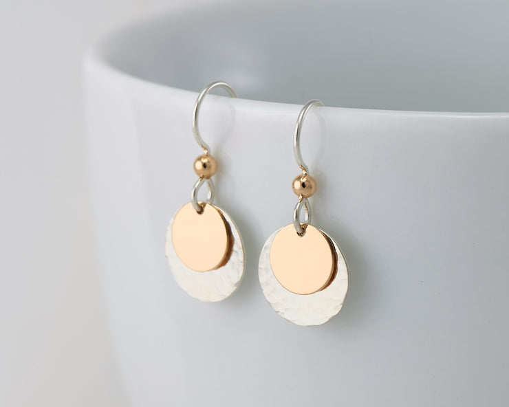 silver and gold disc earrings on white cup