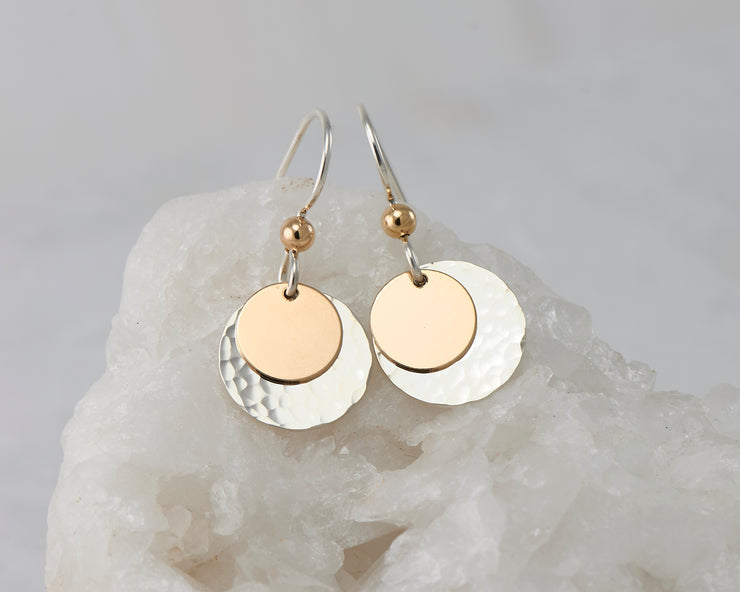 Silver dangle and gold disc earrings on white rock