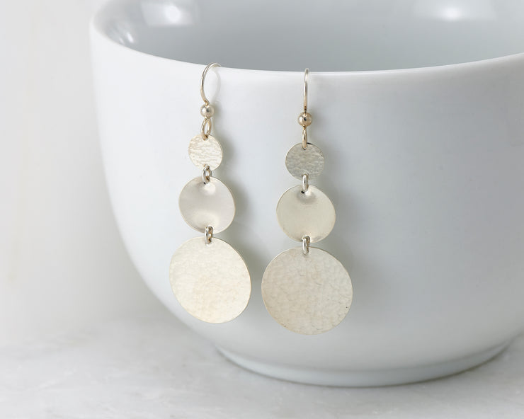 Silver disc earrings hanging from a white cup