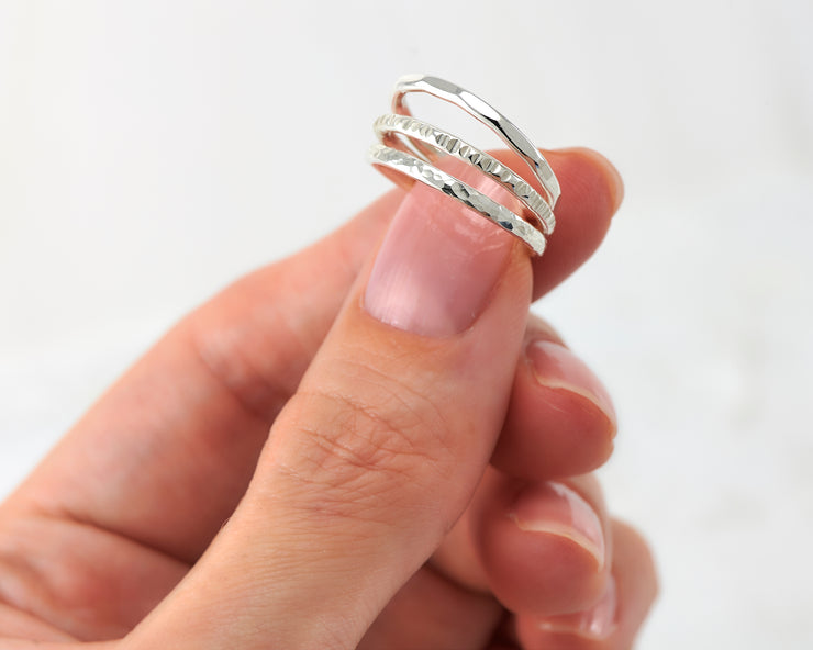 woman holding 3 silver stacking rings of different finishes