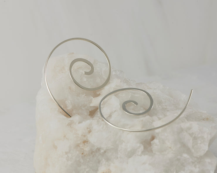 Silver dangle swirl threader earrings on white rock