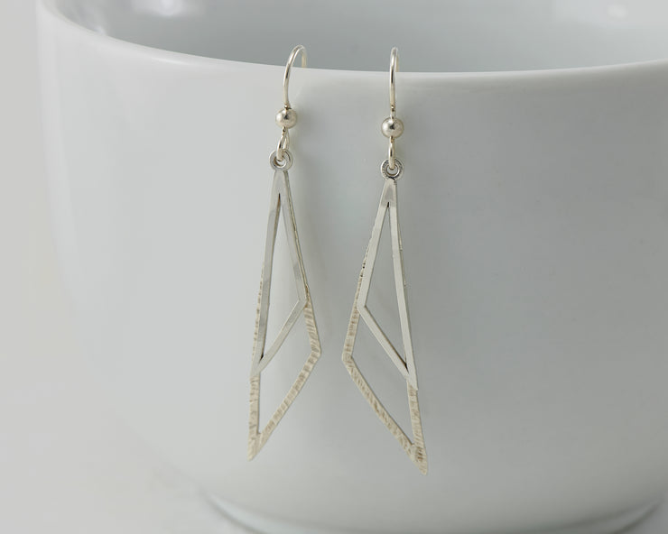 Silver triangle earrings on white cup