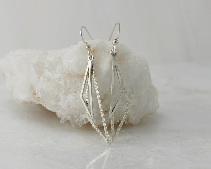 Silver triangle earrings on white rock