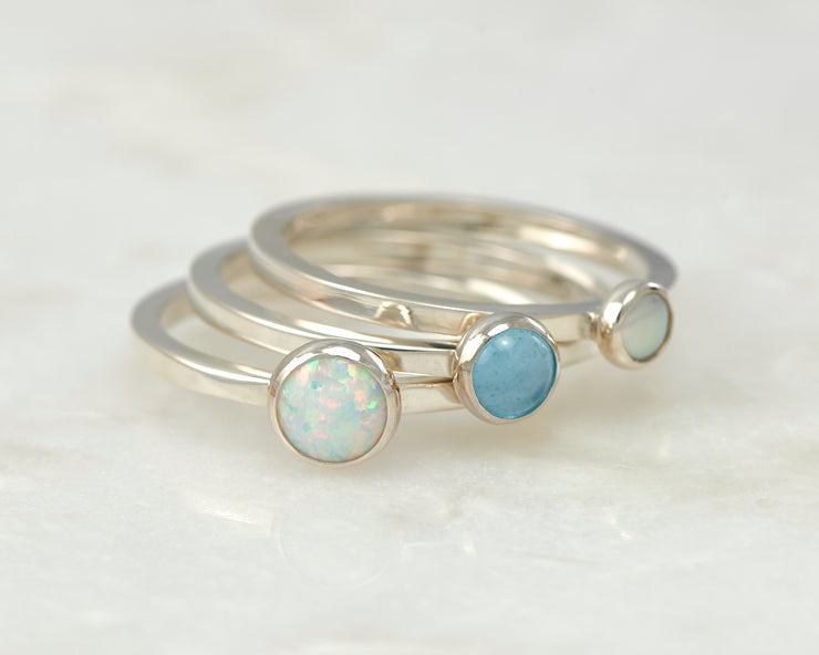 simple opal, pearl, blue topaz silver stacking rings on white marble