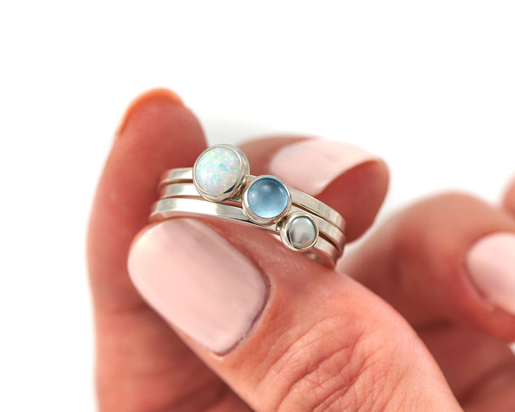 woman holding opal, pearl, blue topaz ring