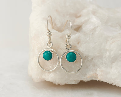 Silver turquoise hoop earrings on white rock